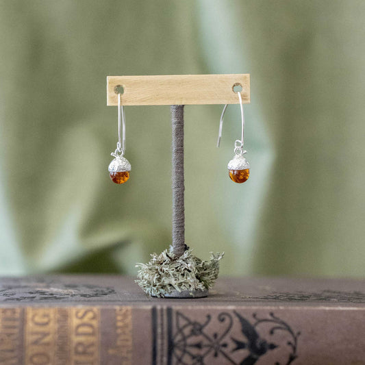Delicate silver amber earrings on a display stand.